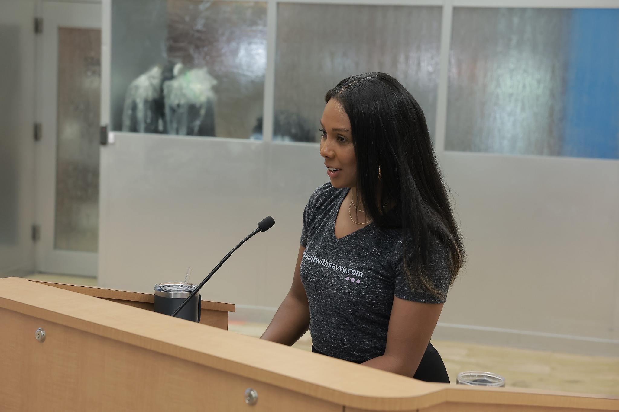 Monique Wingard speaking at a lectern with a microphone.