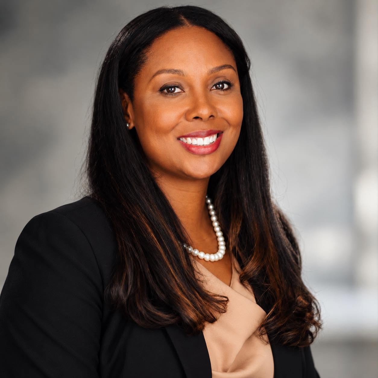 Monique Wingard smiling in a black blazer and pearl necklace.